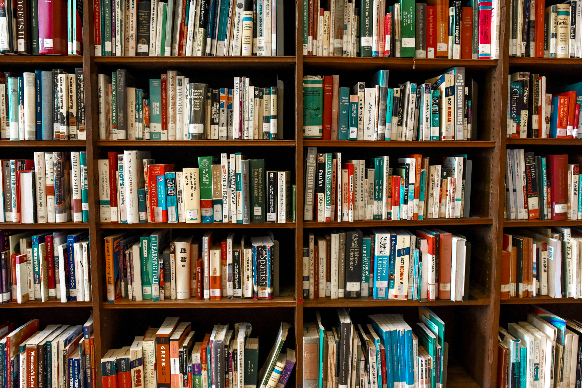 An array of well-worn library books on wooden shelves. Stock image via Pexel.