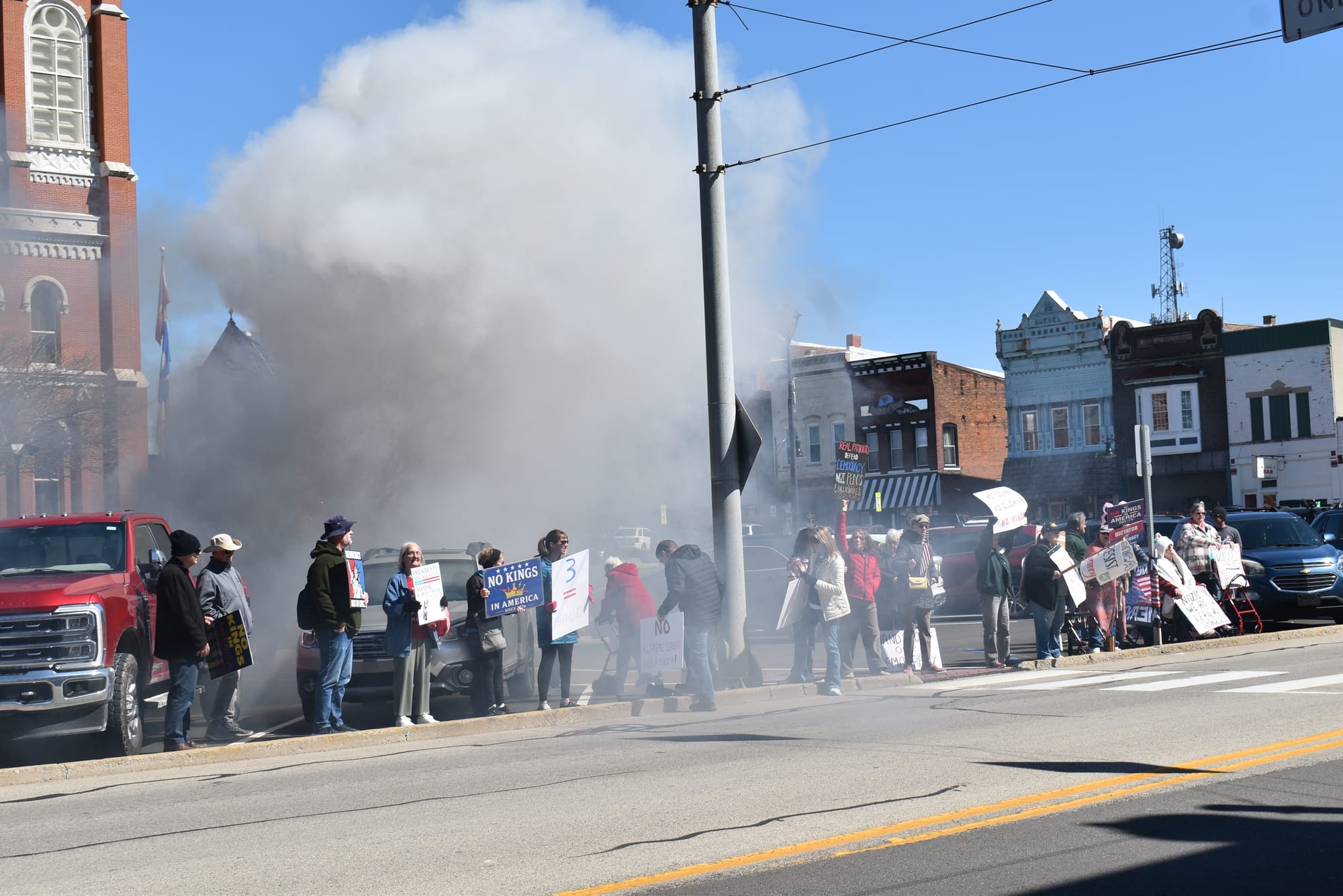 Protesters remain lined up in a plume of smoke along Main Street, Greensburg, Indiana, after a passing pick-up truck "coal rolled" them. Photo by Noelle Maxwell.